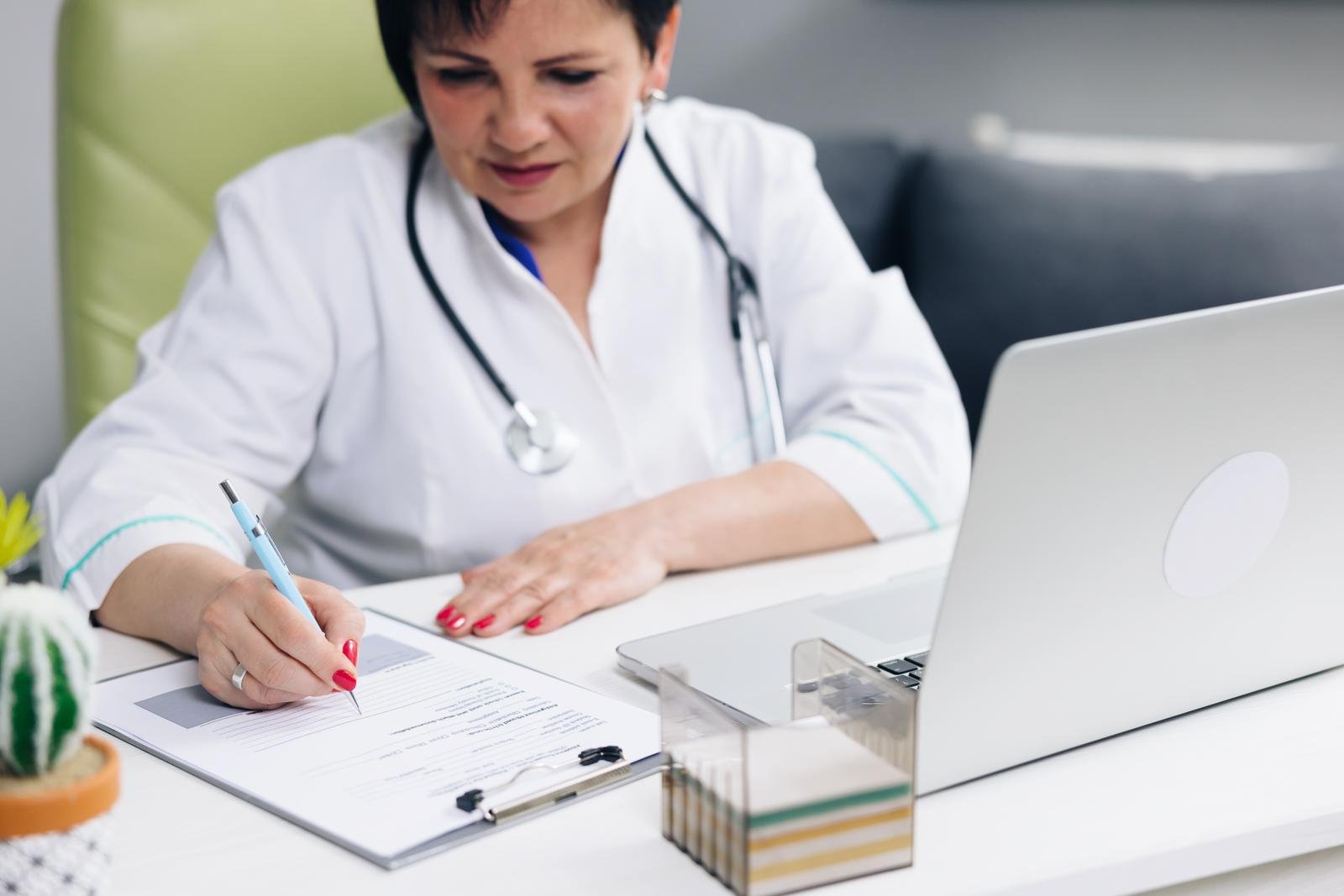 Close up wrinkled female hands writing information in medical registration journal. Old mature doctor therapist working at office, handwriting notes